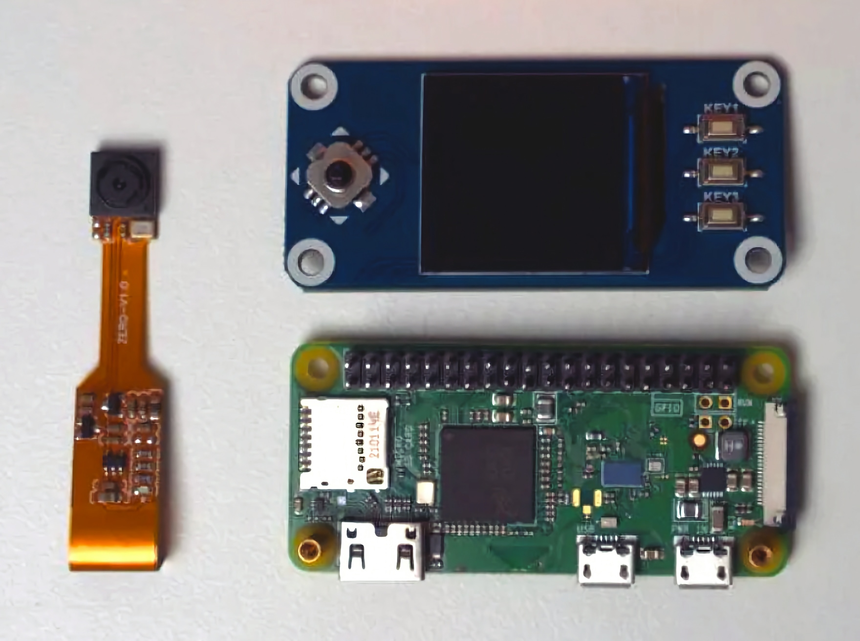 SeedSigner hardware components laid out on a table: a Raspberry Pi Zero board, a camera ribbon cable module, and a WaveShare LCD HAT with joystick and buttons